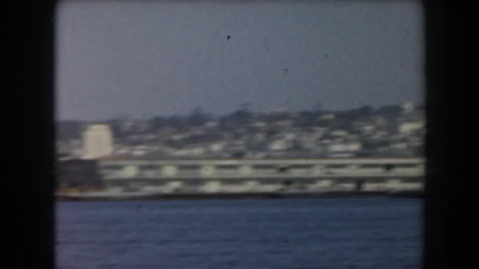 1961 California home-movie frame showing a low waterfront district and distant hillside or shoreline across the bay.