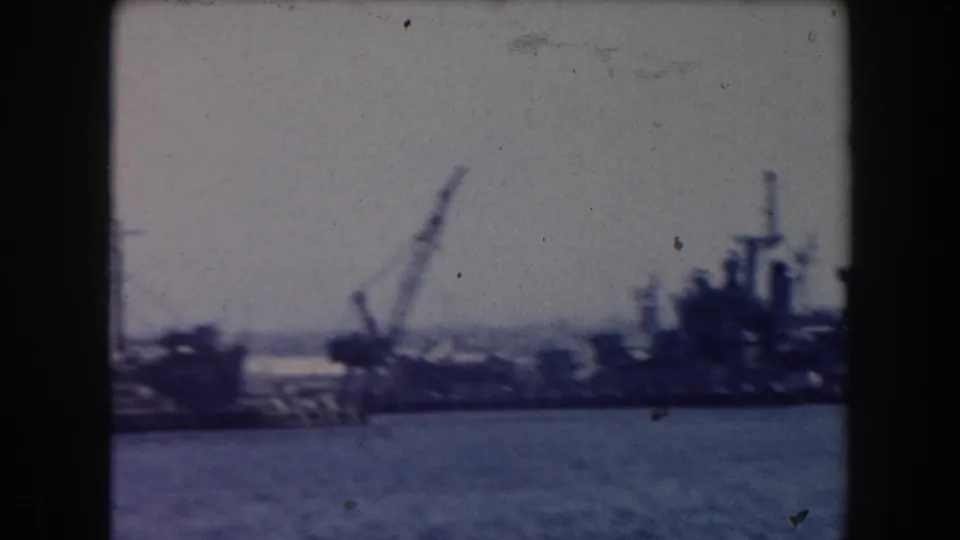 Soft 8mm view of a California harbor shoreline with cranes, dock structures, and moored vessel shapes across the water.