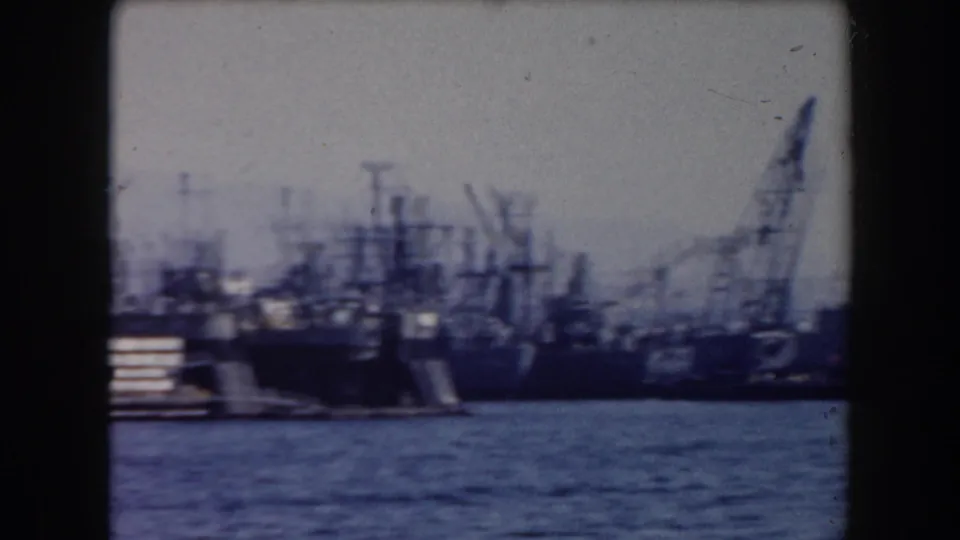 Blue-tinted 8mm view of multiple docked naval vessels and cranes in a California harbor, based on clip metadata.