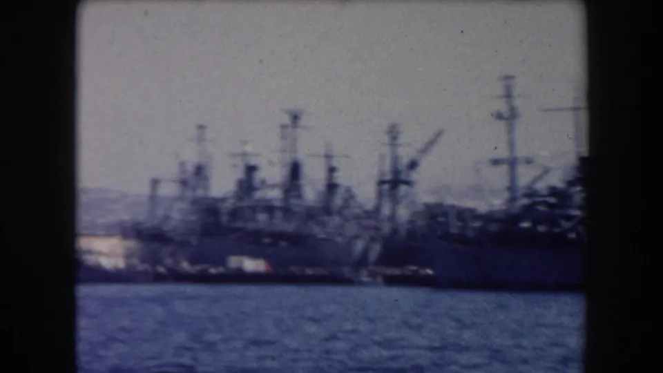Soft-focus final frame with naval ships, tall masts, and harbor water in a blue-tinted California 8mm home movie.