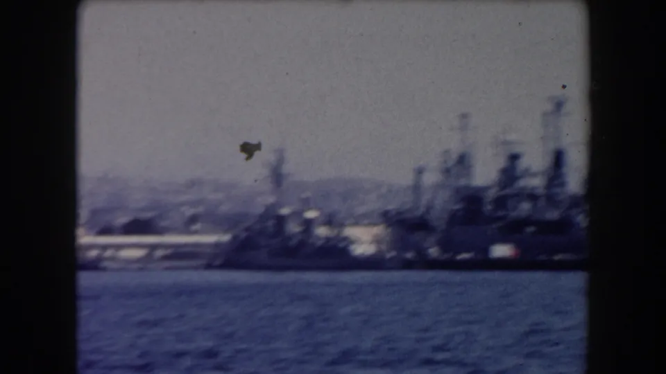 Soft 8mm view of large gray warships anchored in a California harbor in 1961, seen across blue water with distant hills.