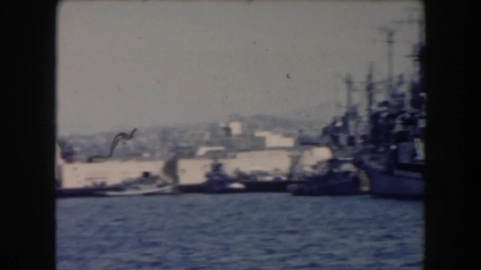 1961 California harbor view with docked naval vessels, blue water, low buildings, and dark 8mm frame borders.