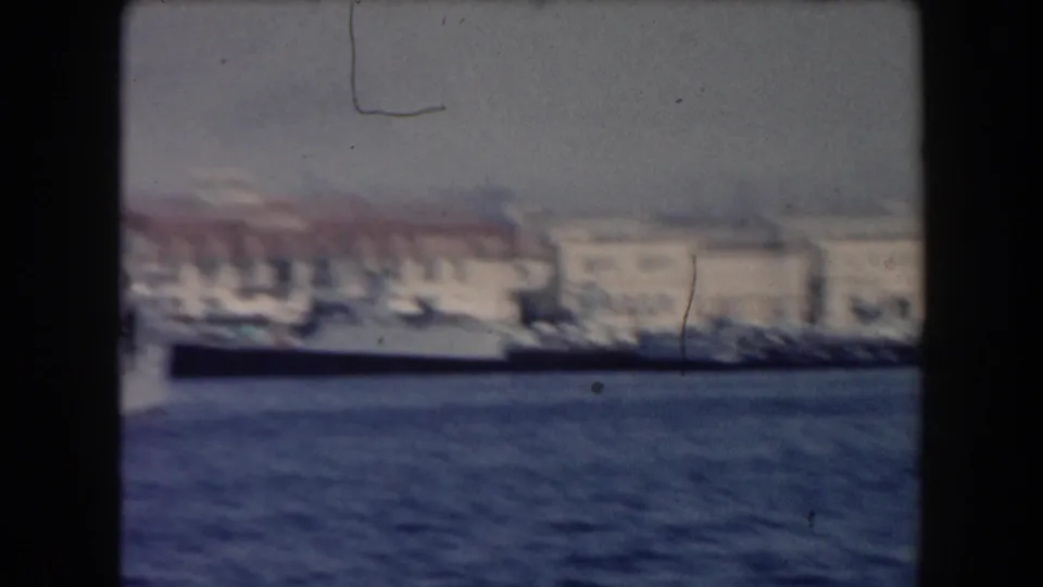 1961 California harbor view with a long docked vessel, pale buildings, shoreline haze, and visible film scratches.