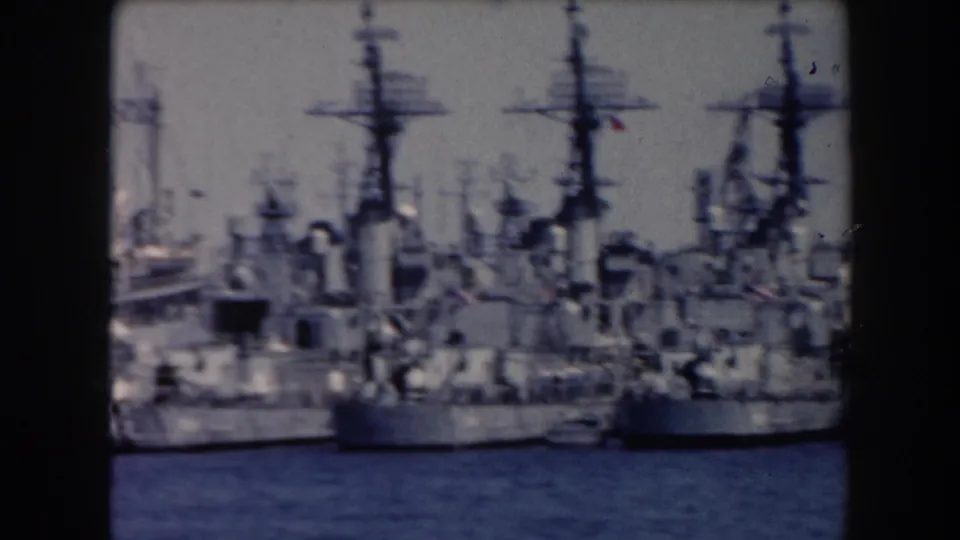 1961 California harbor view of docked naval-looking ships with tall masts and superstructures across the water.