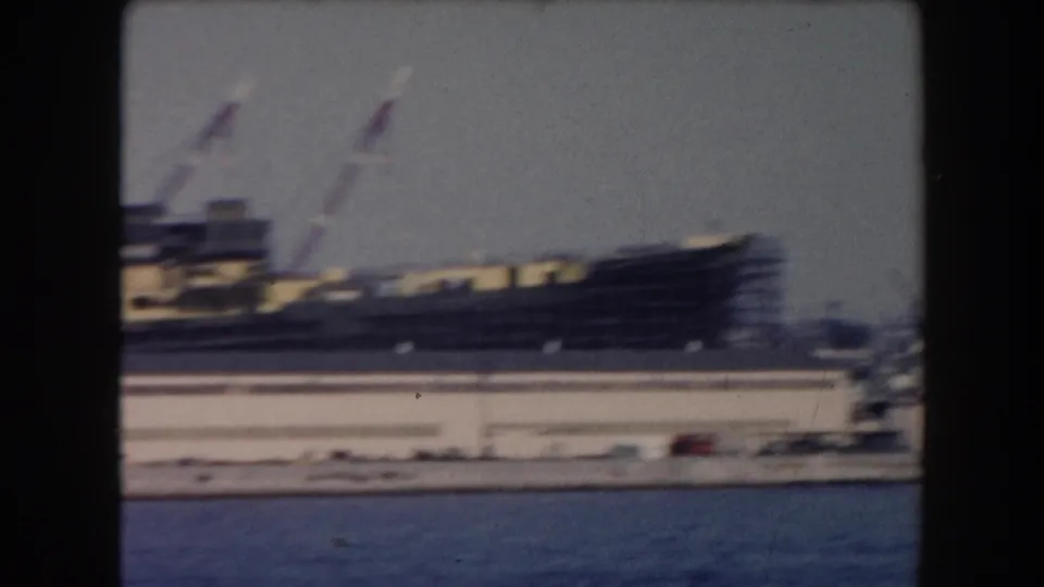 A large transport or cargo vessel appears near cranes and dockside structures in the California harbor footage.