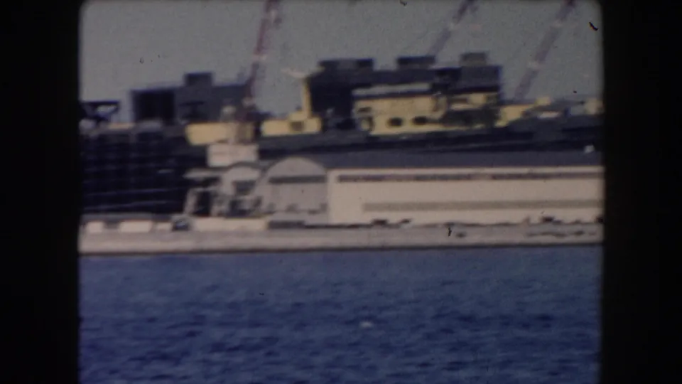 1961 California harbor view from water with docked vessels, low waterfront buildings, and cranes in soft 8mm focus.