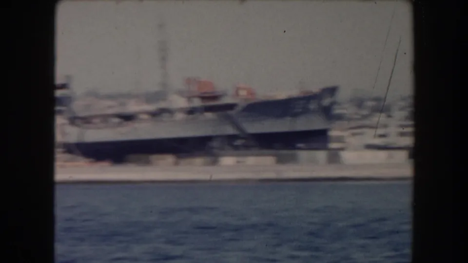Soft 8mm frame of a large naval-looking vessel along the California harbor, viewed from across blue water in 1961.