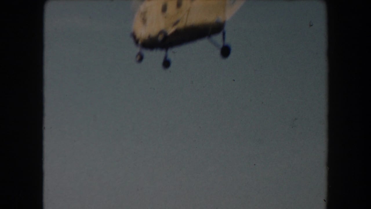 Yellow helicopter partly cropped against a pale sky with dark film frame edges.