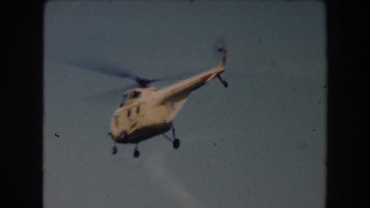 Yellow helicopter in flight against a pale blue sky.