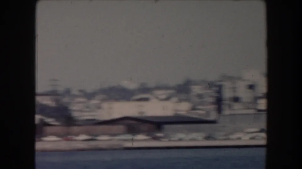 1961 California home-movie frame showing a soft distant shoreline across water with low buildings and haze.