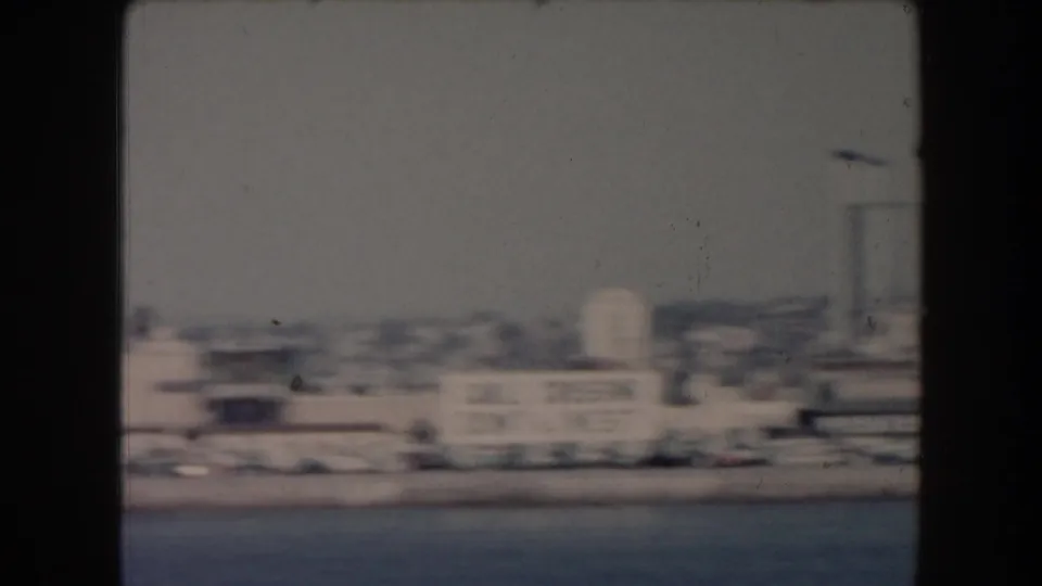 Vintage 8mm coastal cityscape in California, with water in front and soft low-rise shoreline buildings beyond.