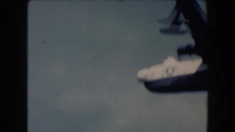 A white-and-dark seaplane appears partly cropped at the right edge of a 1961 California coastal home-movie frame.