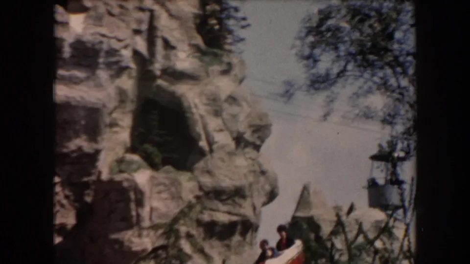 1961 California theme park footage showing artificial rockwork, a dark cave opening, trees, and a small gondola with passengers.