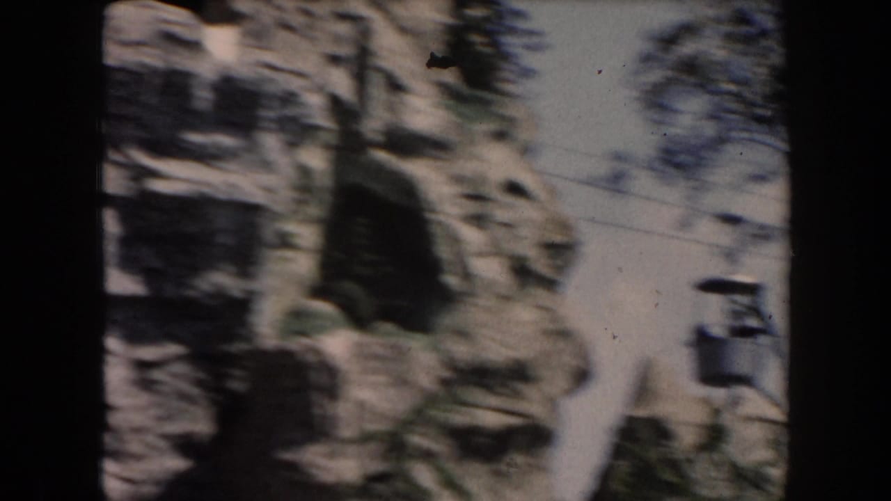 1961 California 8mm frame showing a moving passenger view past artificial cliffs, trees, and shadowed rockwork.