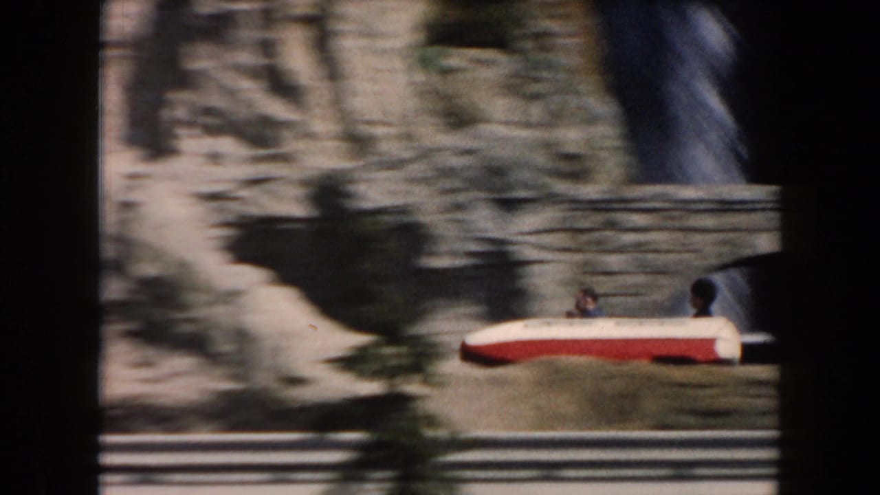 Red-and-white ride car passes along railings beside artificial cliffs.