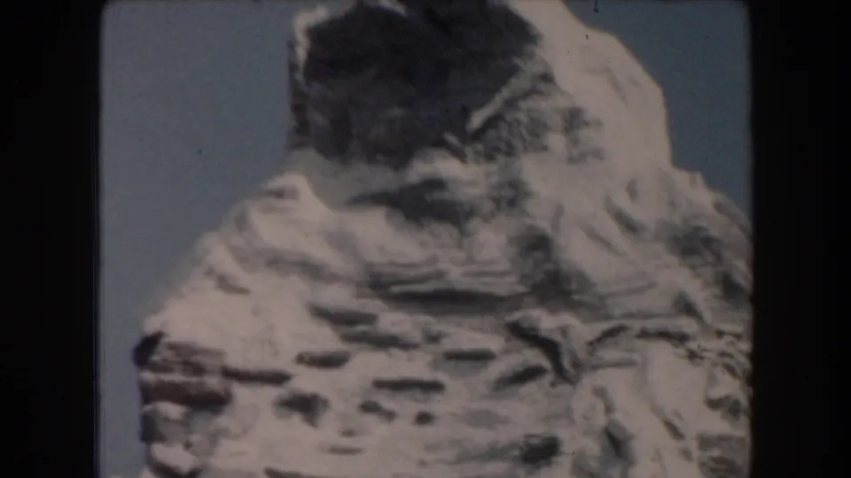 1961 California 8mm frame with a large pale artificial cliff or mountain form rising against blue sky during the ride.