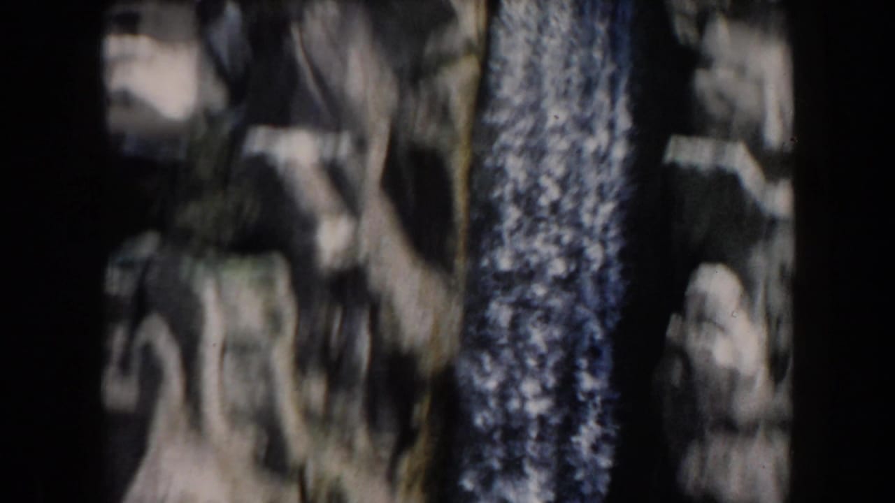Close view of a rocky waterfall area with dark trees or cliff shadows.