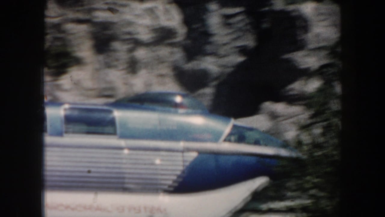Blue and silver monorail entering frame beside a rocky wall.