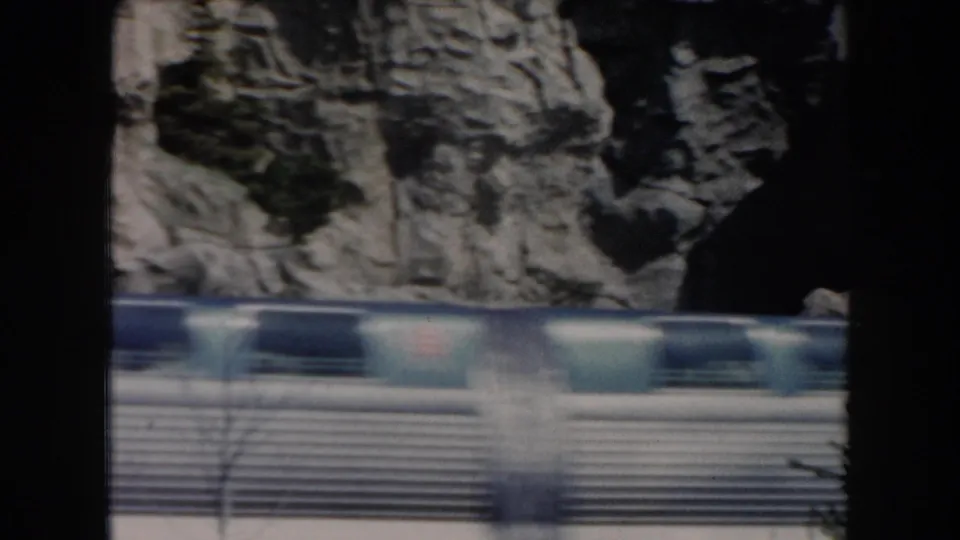A blue and silver monorail moves quickly across the frame against pale rock formations, with motion blur from the 8mm footage.