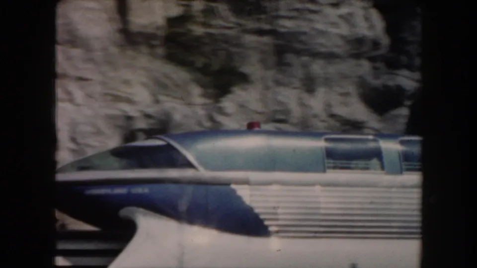 Close 8mm view of the blue and silver monorail cab and side windows passing a rocky wall in California.