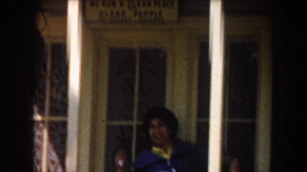Woman sits on a porch bench behind vertical columns.