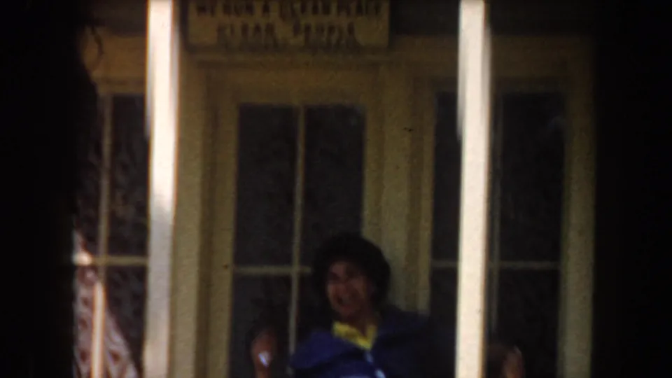 A woman in bright 1960s clothing sits on a porch bench, partly framed by white columns and glass doors.