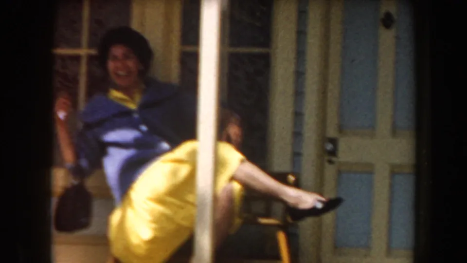 The woman smiles toward the camera while seated on a porch bench, her yellow skirt catching the sunlight.