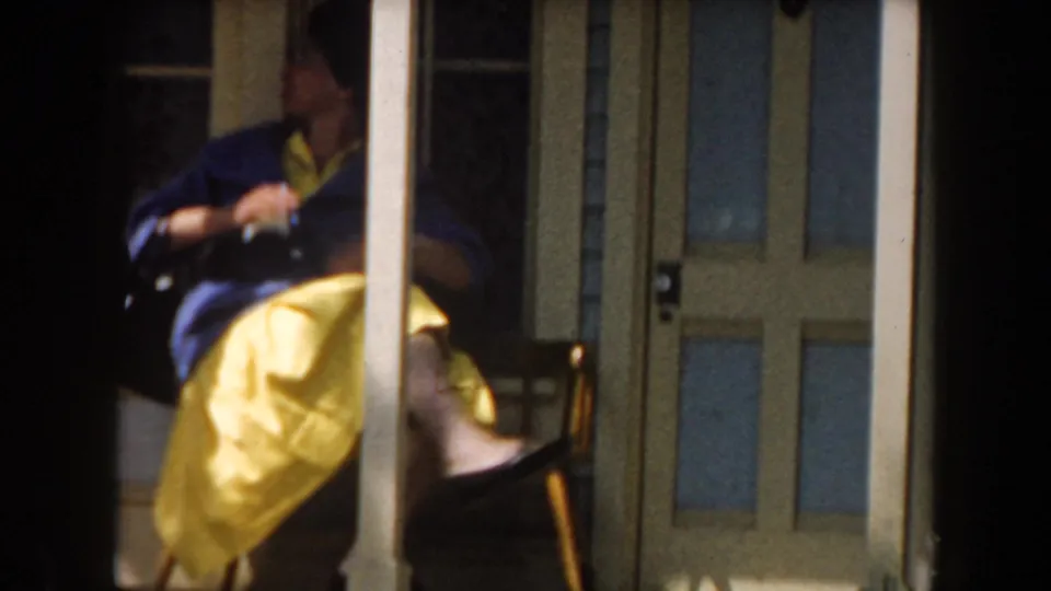 The seated woman turns sideways on the porch bench, with a column crossing the frame and glass-paneled doors behind her.