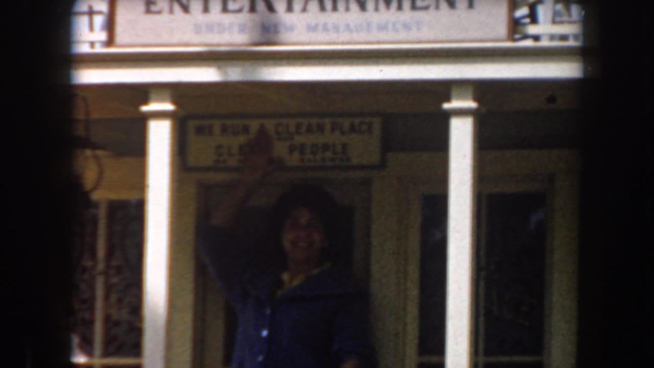 Woman gestures beneath an entertainment sign on a porch-fronted building.