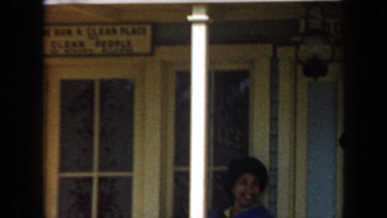 Woman partly visible on a porch beside columns and a storefront sign.