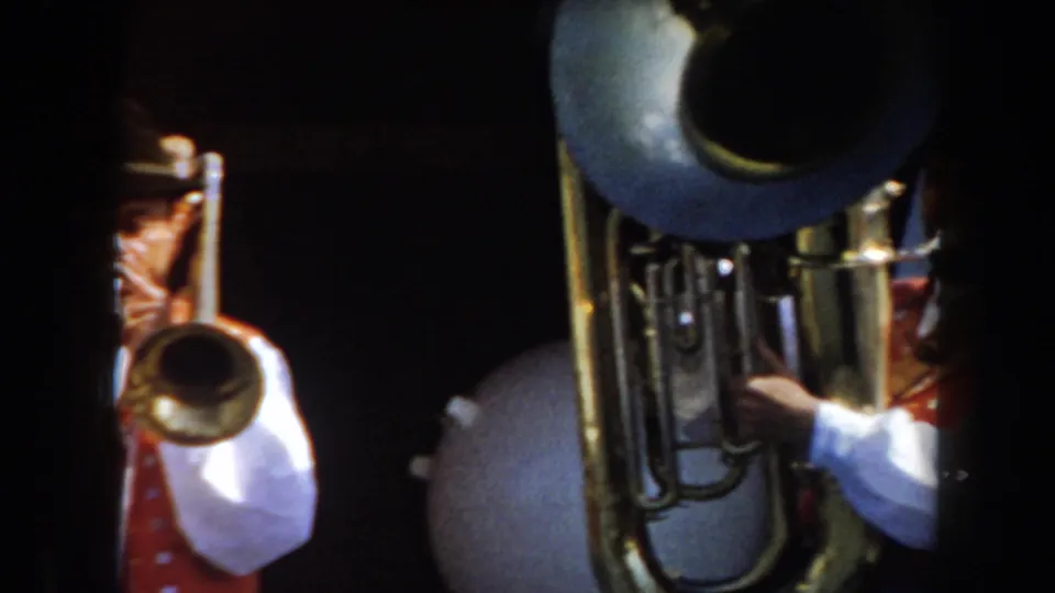 1961 California 8mm frame showing brass musicians in traditional German-style attire, with a large tuba bell near the center.