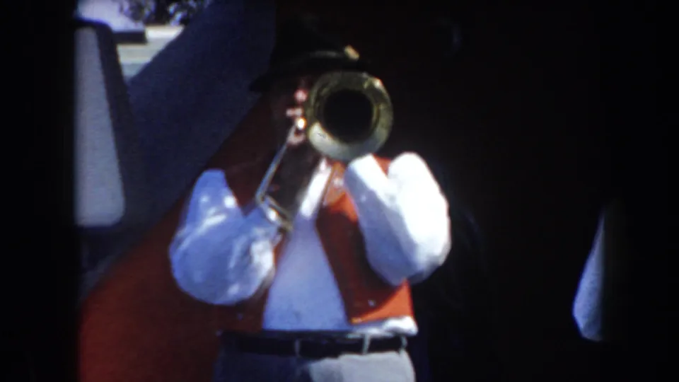 1961 California frame of a trombone player in German-style attire, partially framed by dark edges and other band members.
