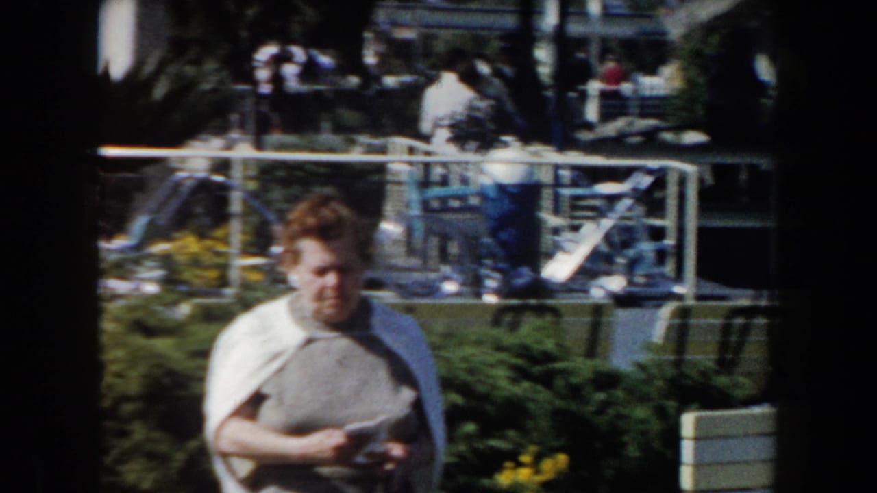 Woman in gray sweater and white shawl walking through a sunny garden.