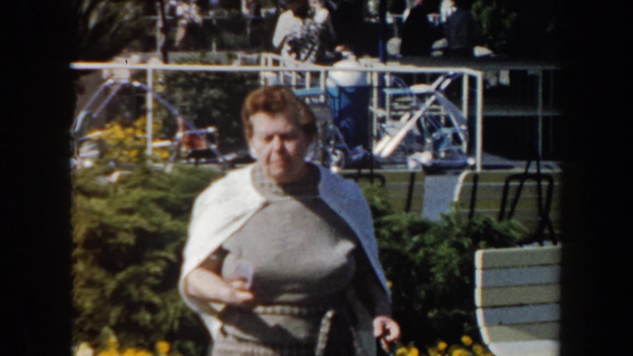 Woman walking closer to camera beside shrubs and yellow flowers.