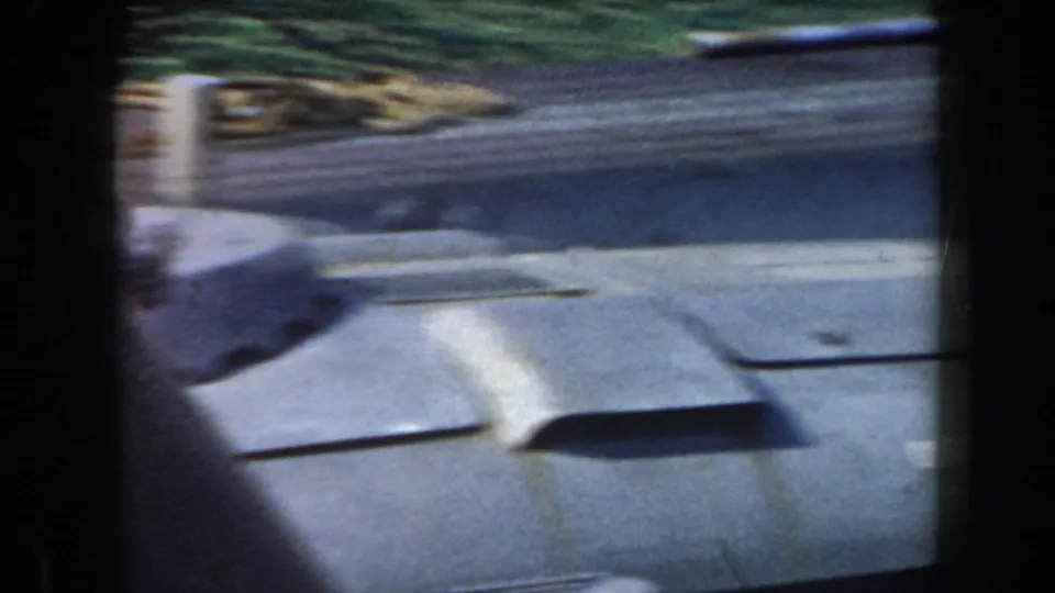 A close 8mm view of a gray ship deck in California, with raised vent or hatch shapes and shoreline greenery beyond.