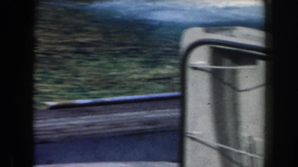 1961 home-movie frame showing a rounded gray ship structure beside water, with shoreline greenery in the background.