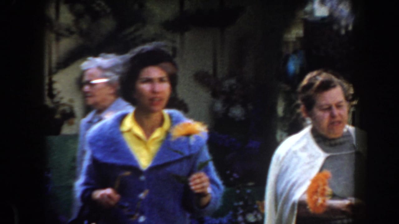 Two adult women walking in a garden, one in a blue jacket and one in a white shawl.