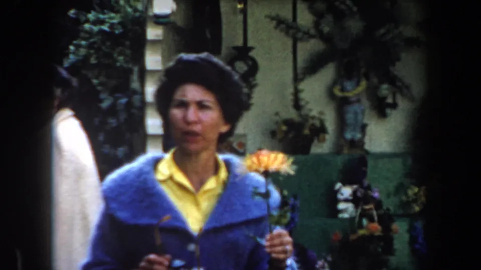 An adult woman in a blue jacket and yellow shirt faces the camera while holding stems in a California garden setting.
