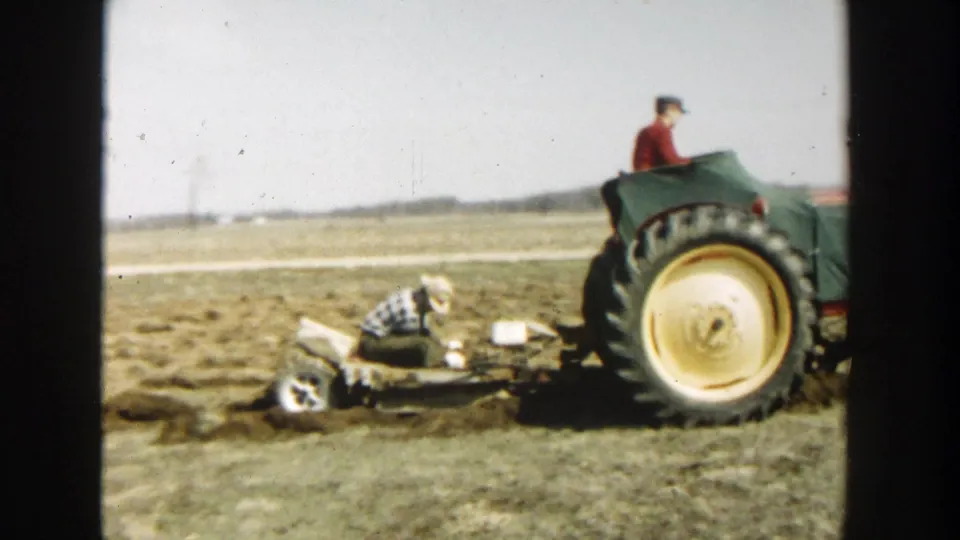 In the 1954 Wisconsin Dells footage, the tractor continues across the field while a man in plaid works near the trailing implement.