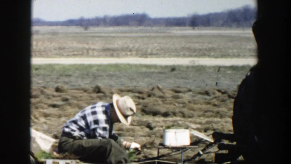 Soft 8mm frame of a farmer crouched on farm equipment during apparent crop gathering in 1954 Wisconsin Dells.