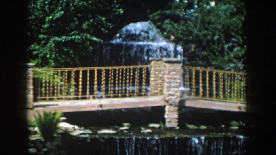 1954 Wisconsin Dells home-movie frame with water spilling over a domed stone feature behind a railing and bridge.