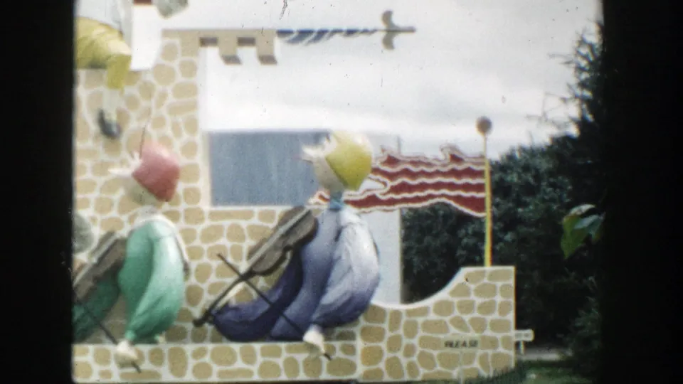 1954 Wisconsin Dells 8mm frame showing two colorful storybook figures near a castle-like wall, with an American flag and knight detail above.