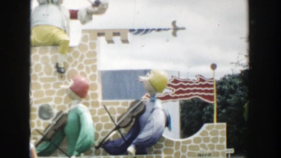 1954 Wisconsin Dells frame of a whimsical castle display with two fiddle-playing figures, a small flag, and soft faded 8mm color.