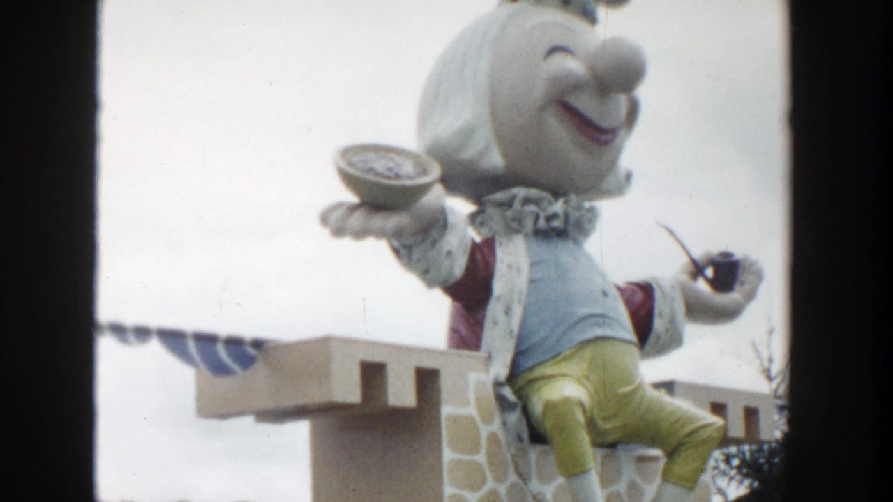 1954 Wisconsin Dells 8mm frame showing a large crowned puppet seated on a castle-like roadside display with a bowl and pipe.