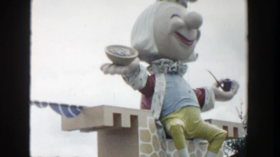 1954 Wisconsin Dells 8mm frame showing a large crowned puppet seated on a castle-like roadside display with a bowl and pipe.