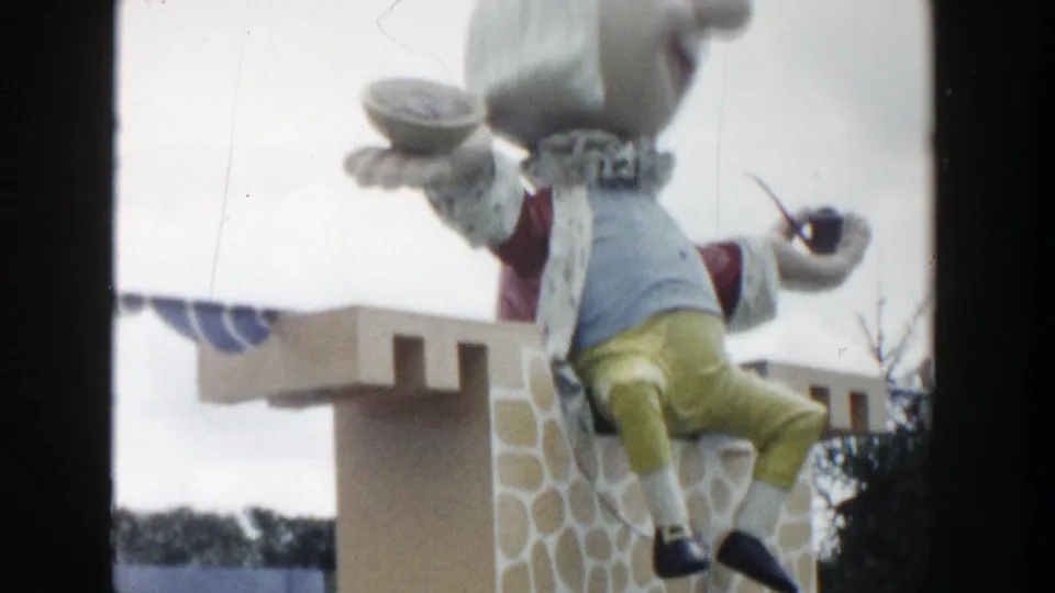 Soft 8mm close framing of the Wisconsin Dells puppet display, emphasizing the costume, bowl, pipe, and faux-stone tower.