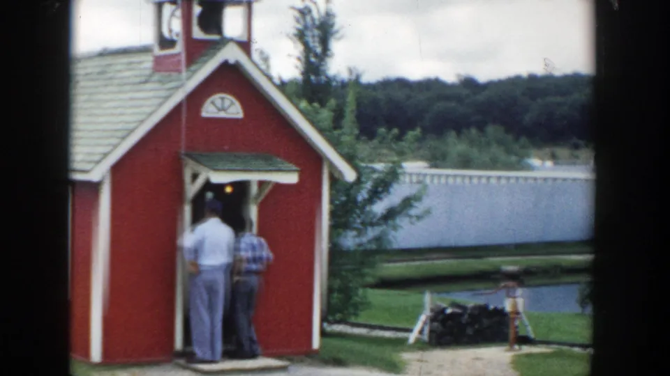 1954 Wisconsin Dells home-movie view of a red schoolhouse facade with two men seen from behind at the doorway.