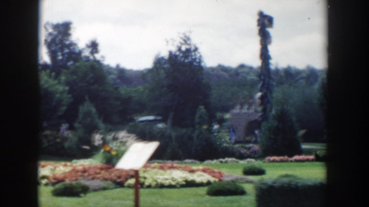 Formal garden with lawns, flowerbeds, trees, a signboard, and a tall pole-like sculpture.