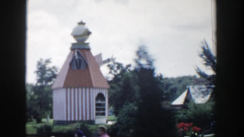 1954 Wisconsin Dells garden frame showing a small striped structure with a red roof and spherical top, surrounded by trees and flowers.
