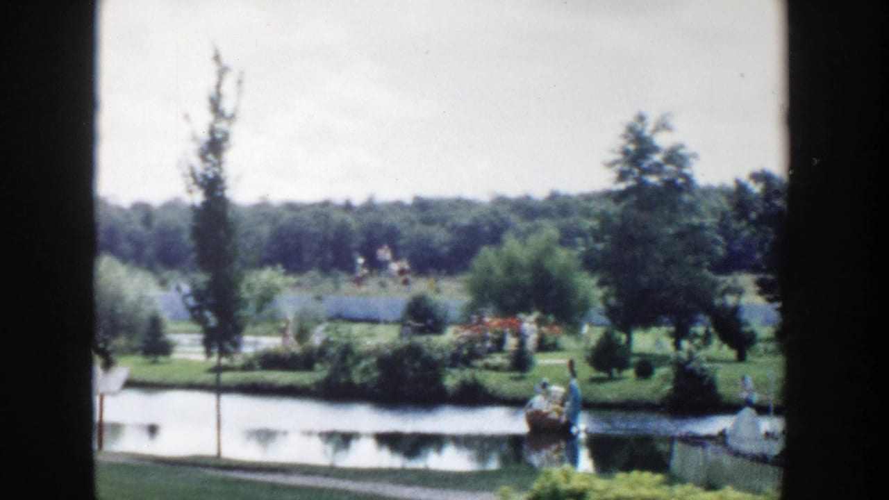 1954 Wisconsin Dells home-movie view of a pond, green lawn, trees, and small distant tourist figures framed by dark film edges.